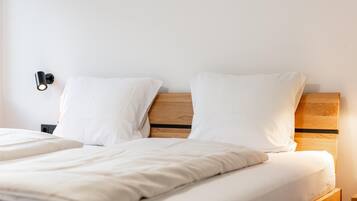A neatly made bed with white bedding, a wooden headboard, and a nightstand with a lamp.