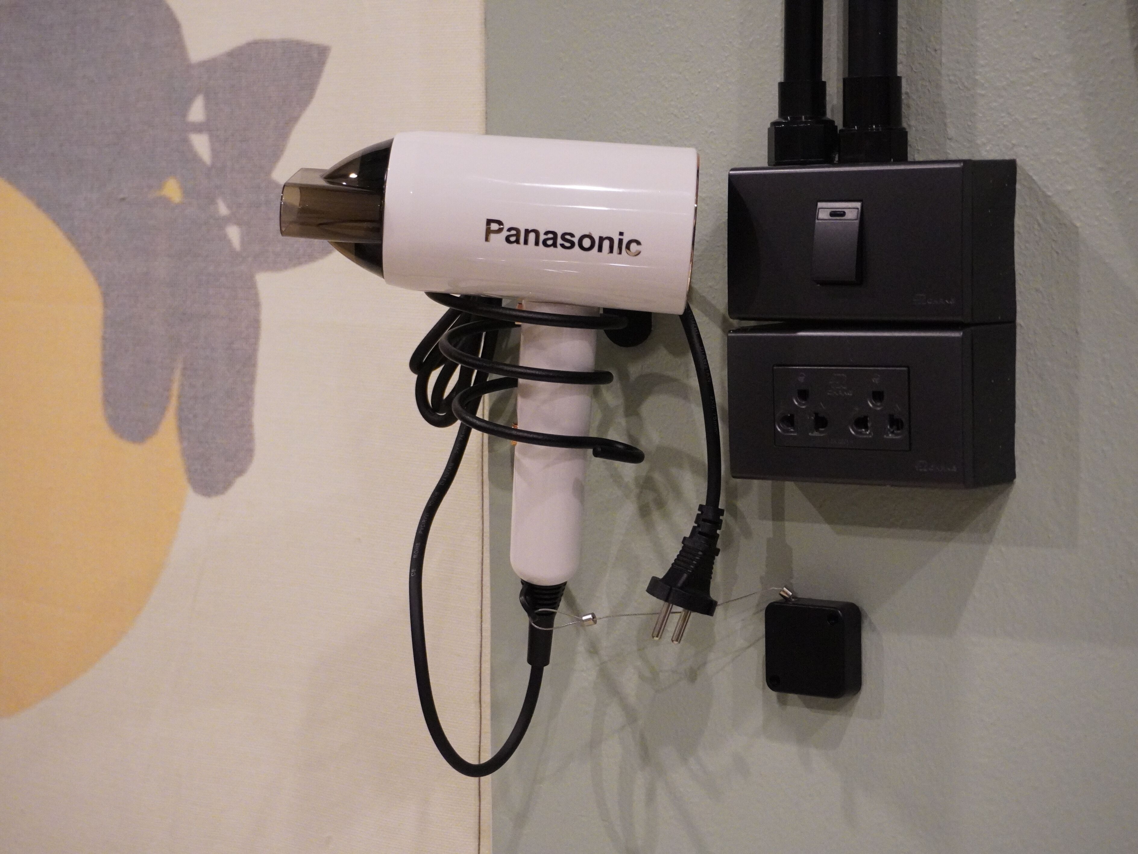 A Panasonic hair dryer mounted on a wall, connected to a power strip with multiple outlets.
