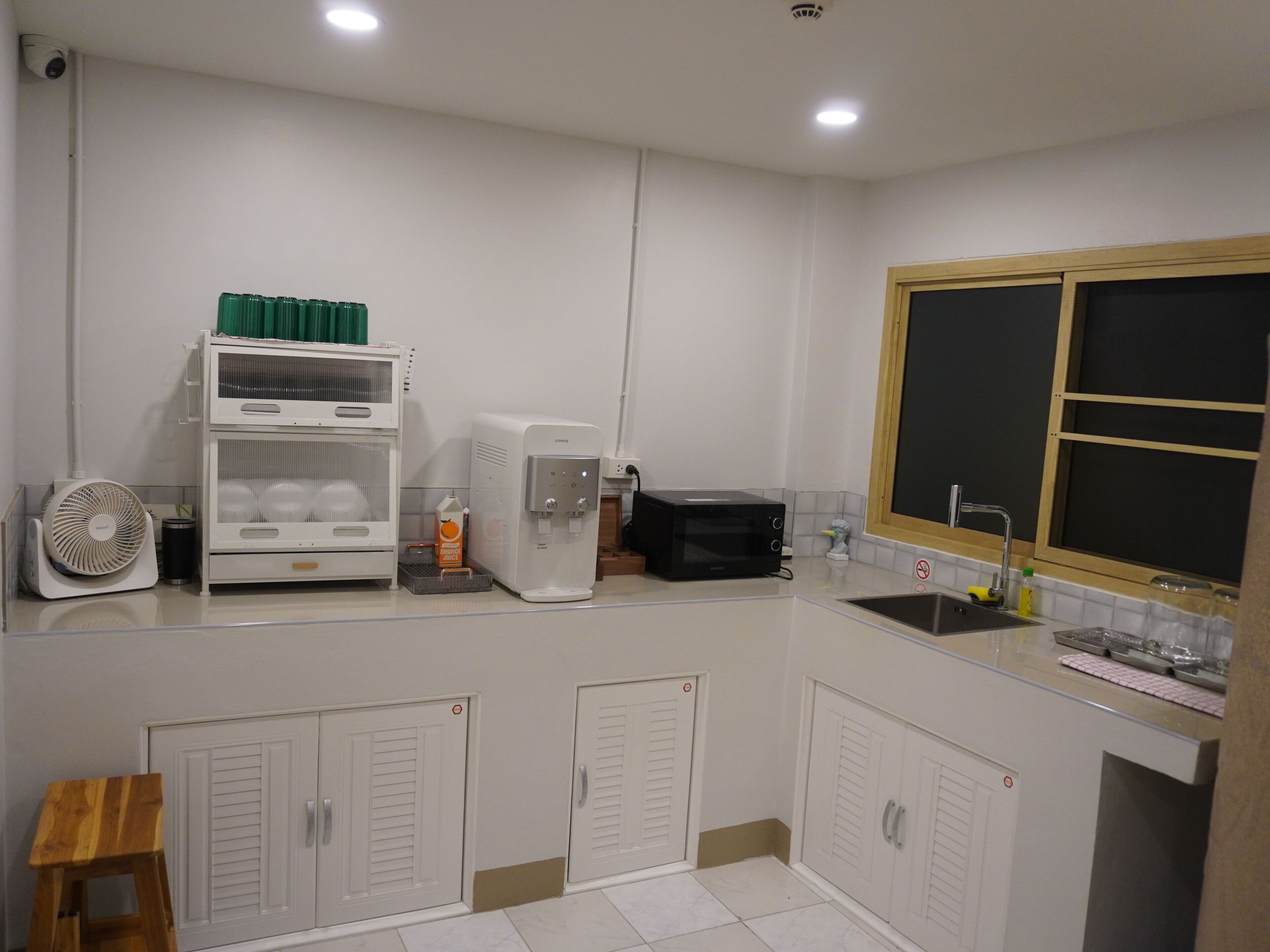 Cocina compacta con microondas, dispensador de agua, ventilador y un lavamanos pequeño.