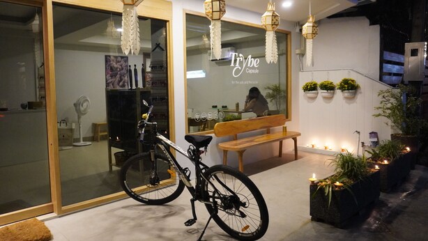 A modern building with a glass facade, a bench, a bicycle, and hanging lanterns. - Trybe Capsule Hostel Chiang Mai (Chiang Mai)
