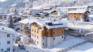 Ett snötäckt bostadsområde med moderna flerfamiljshus, inklusive ett framträdande trähus med balkonger.