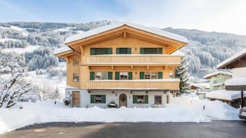Un edificio de madera de dos pisos con techo inclinado, rodeado de árboles y montañas cubiertas de nieve.