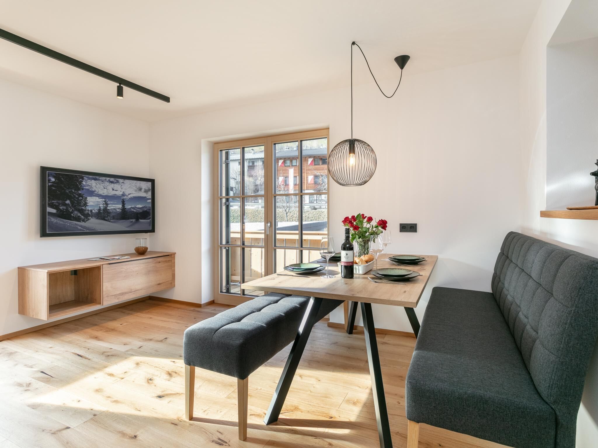 Un comedor moderno y bien iluminado con una mesa de madera, bancos y un ventanal con vistas al exterior.
