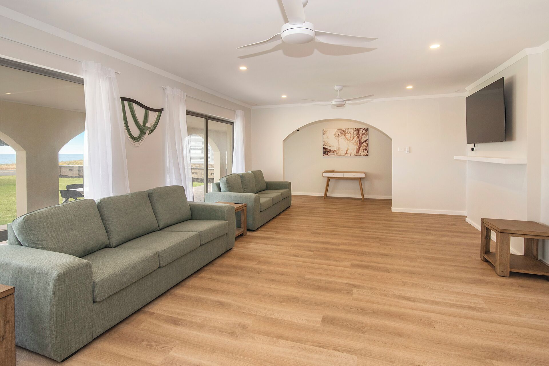 A spacious living area with a large sofa, a coffee table, and a TV mounted on the wall.