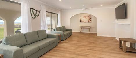 A spacious living area with a large sofa, a coffee table, and a TV mounted on the wall.