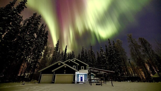 Une maison avec un garage et une véranda, entourée de neige et d’arbres.