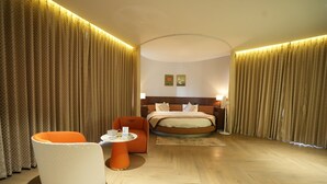 A hotel room with a bed, a white armchair, a small table, and curtains. - Hotel Four Point Corner (Pali)
