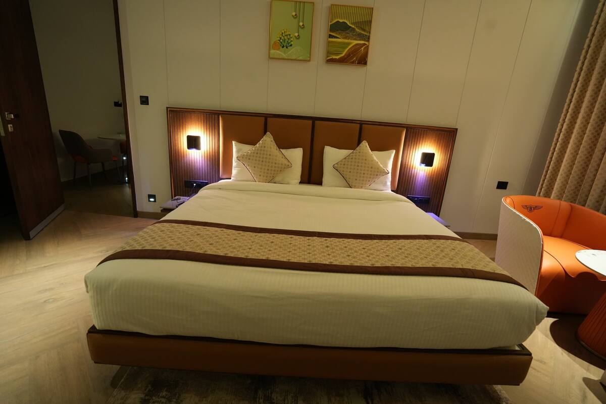 Una habitación de hotel con una cama grande, un cabecero de madera, dos lámparas de pared y una mesita con una silla.