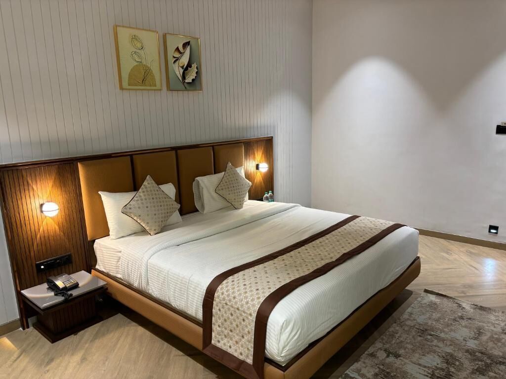 Una cama bien hecha con cabecera de madera, dos lámparas de noche y una mesita de noche con un teléfono y una botella.