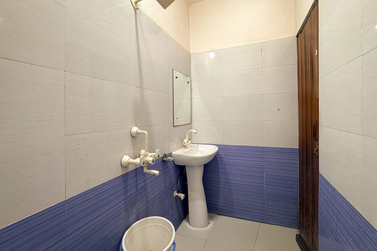 Un baño con azulejos blancos y azules, un lavamanos pedestal, un espejo y una puerta de madera.