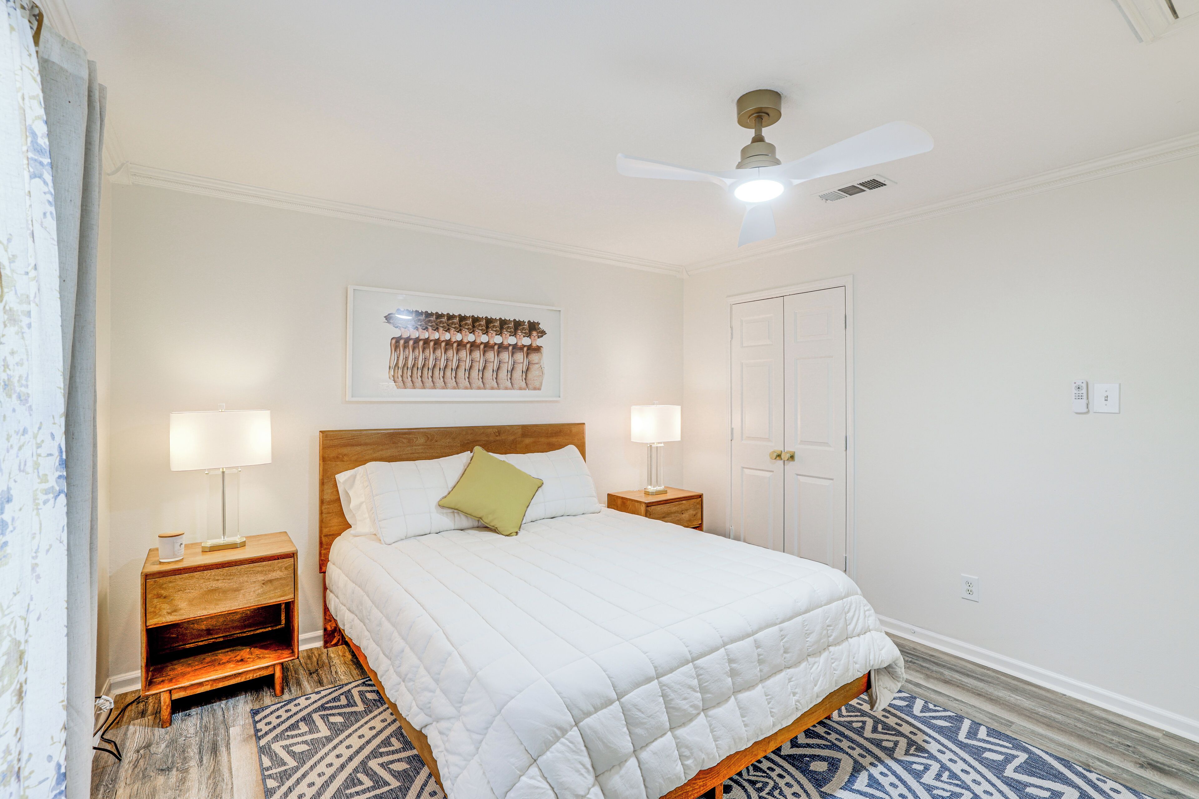 Une chambre à coucher bien rangée, avec un lit, deux tables de chevet dotées de lampes, un ventilateur de plafond et un tapis à motifs.