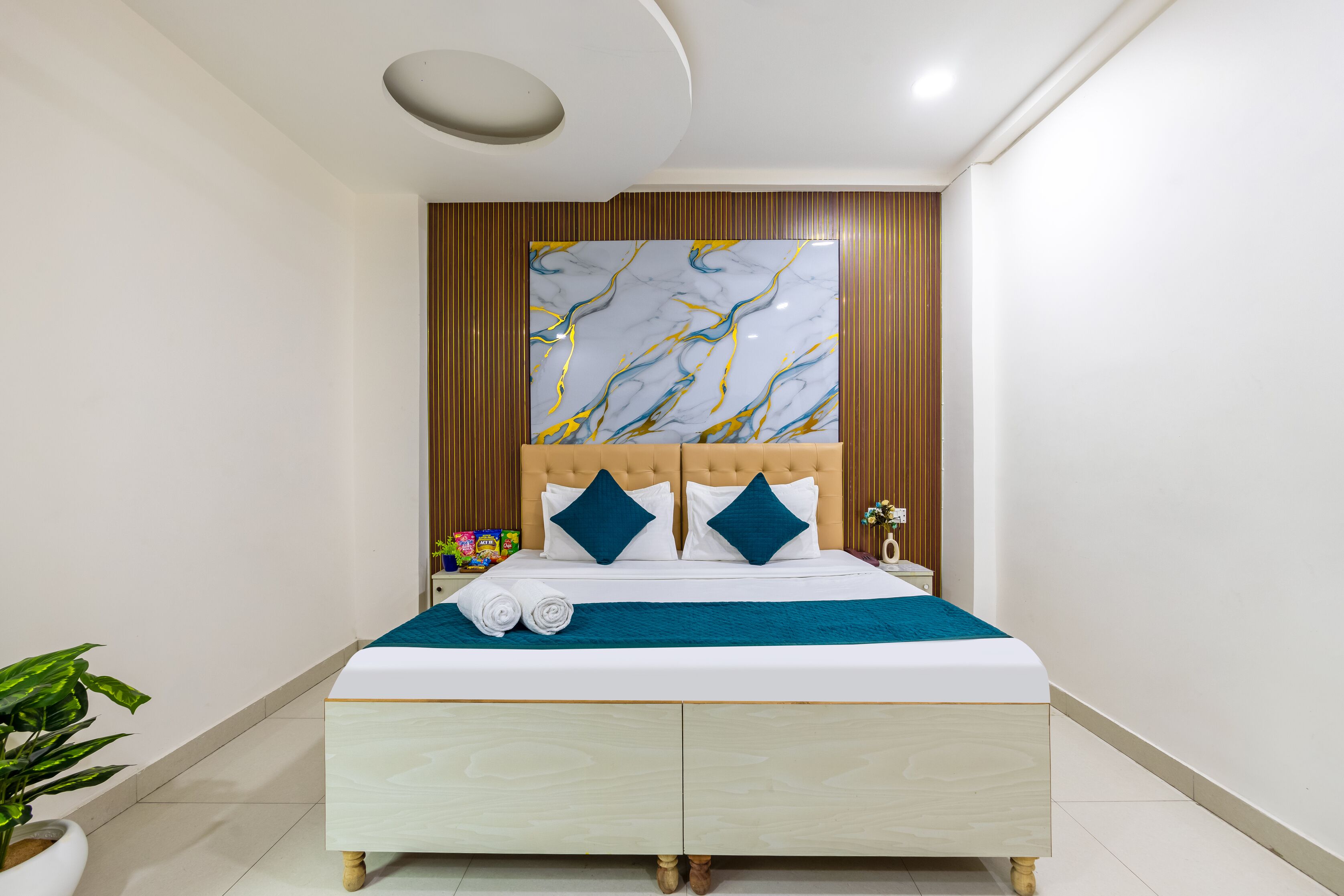A modern hotel room with a large bed, wooden paneling, and a marble artwork above the bed.