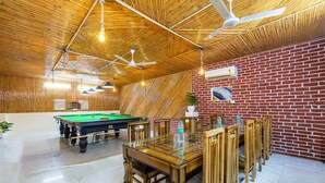 A billiards room with a pool table, wooden chairs, and a brick wall. - Hotel Admire Expressway BY ASPL (Noida)
