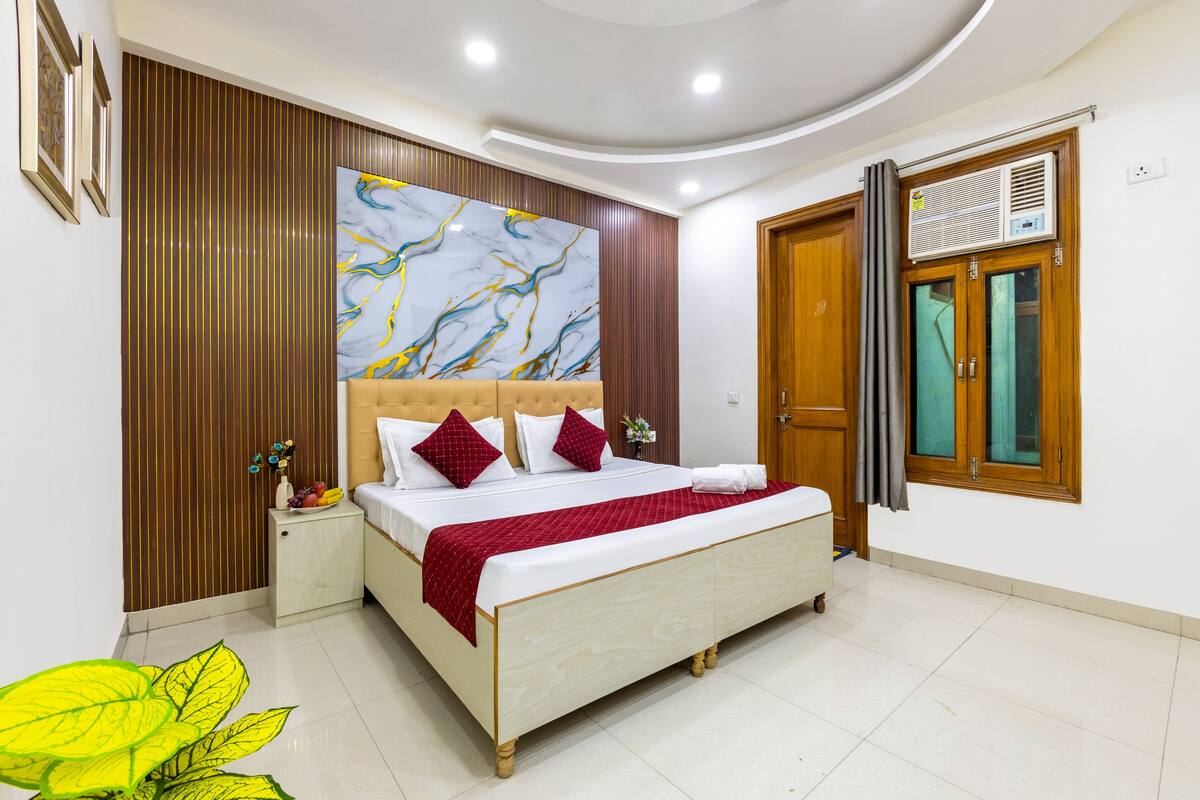 Un dormitorio moderno con una cama grande, paneles de madera, un cuadro abstracto de gran tamaño y una ventana con equipo de aire acondicionado.
