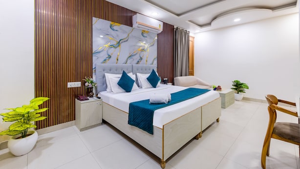 A modern hotel room with a large bed, a ceiling fan, a wall-mounted air conditioner, and a potted plant. - Hotel Admire Expressway BY ASPL (Noida)