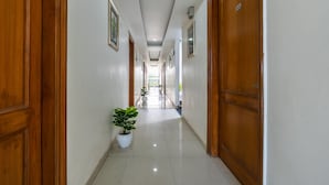 A corridor with wooden doors, white walls, and potted plants. - Hotel Admire Expressway BY ASPL (Noida)