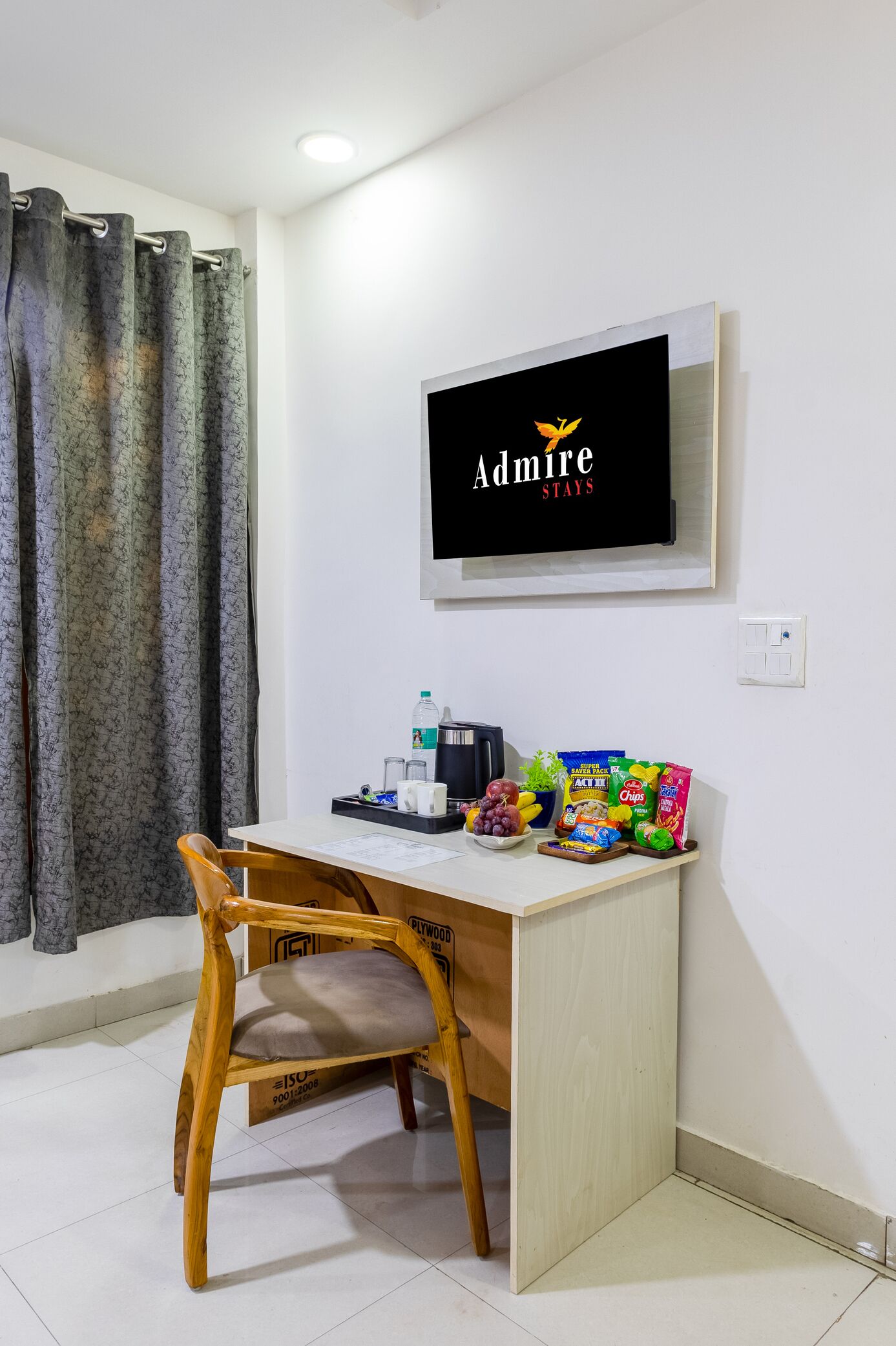 Ein Zimmer mit einem Holztisch, einem Stuhl, einem an der Wand befestigten Fernseher sowie Snacks und Getränken auf dem Tisch.