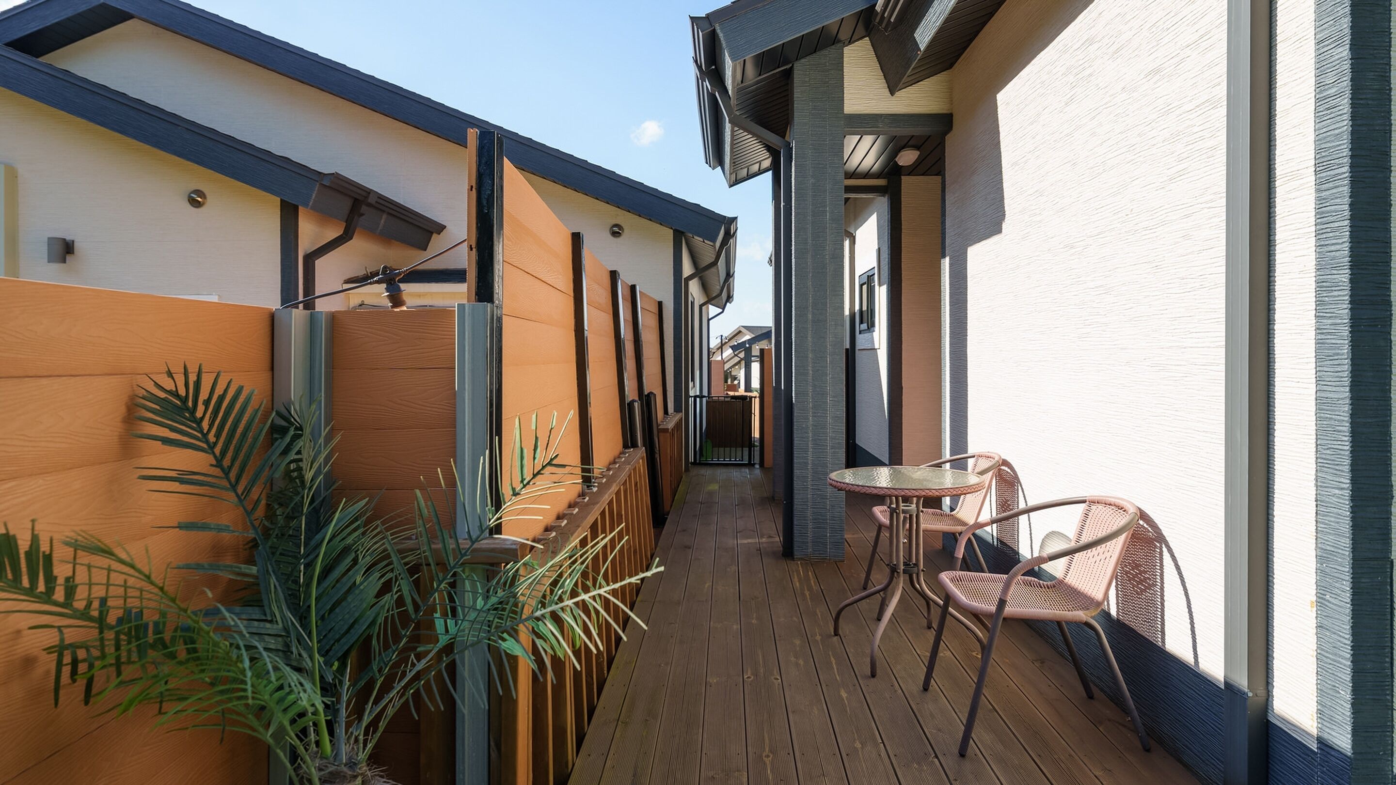 Une terrasse en bois avec une table et des chaises, entourée de plantes et bordée d’un bâtiment au design moderne.