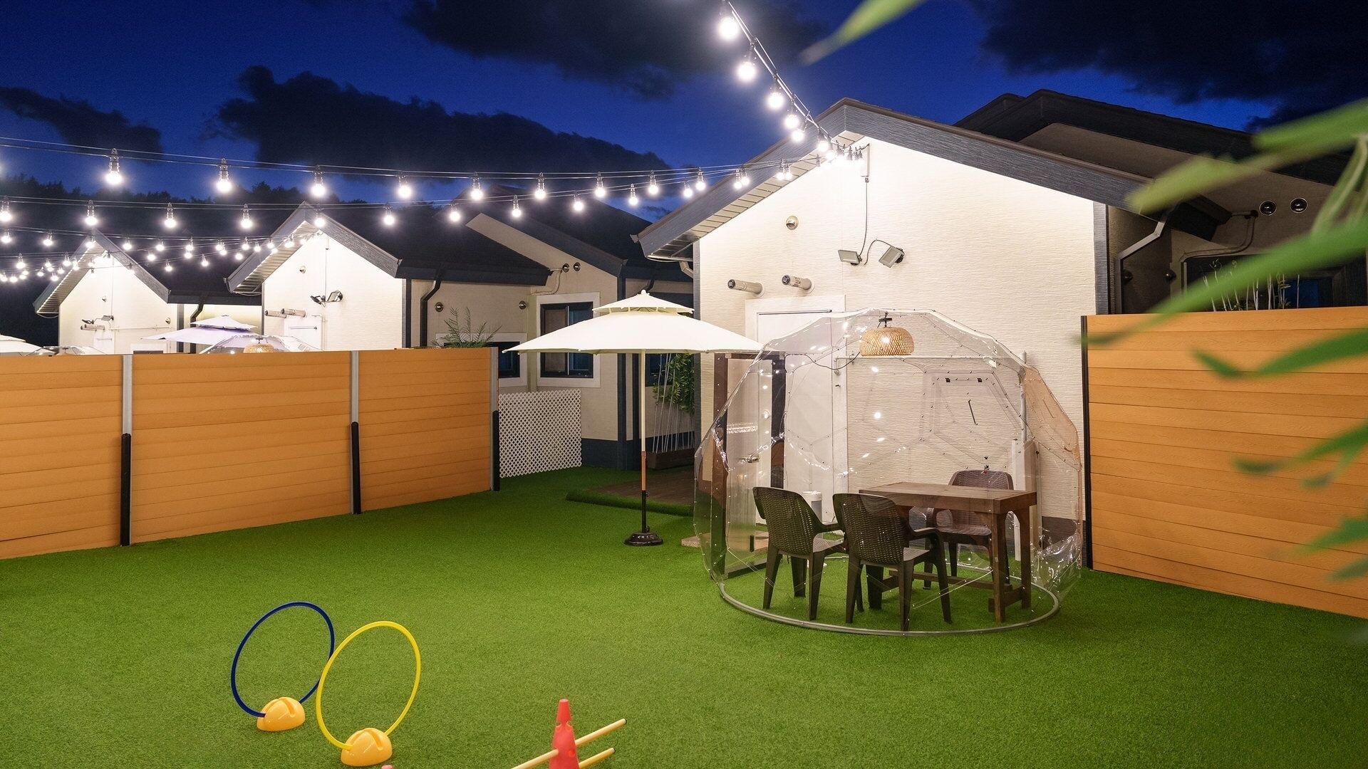 A backyard with artificial grass, a covered seating area, and string lights.