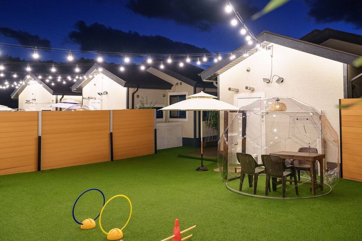 A backyard with artificial grass, a covered seating area, and string lights.