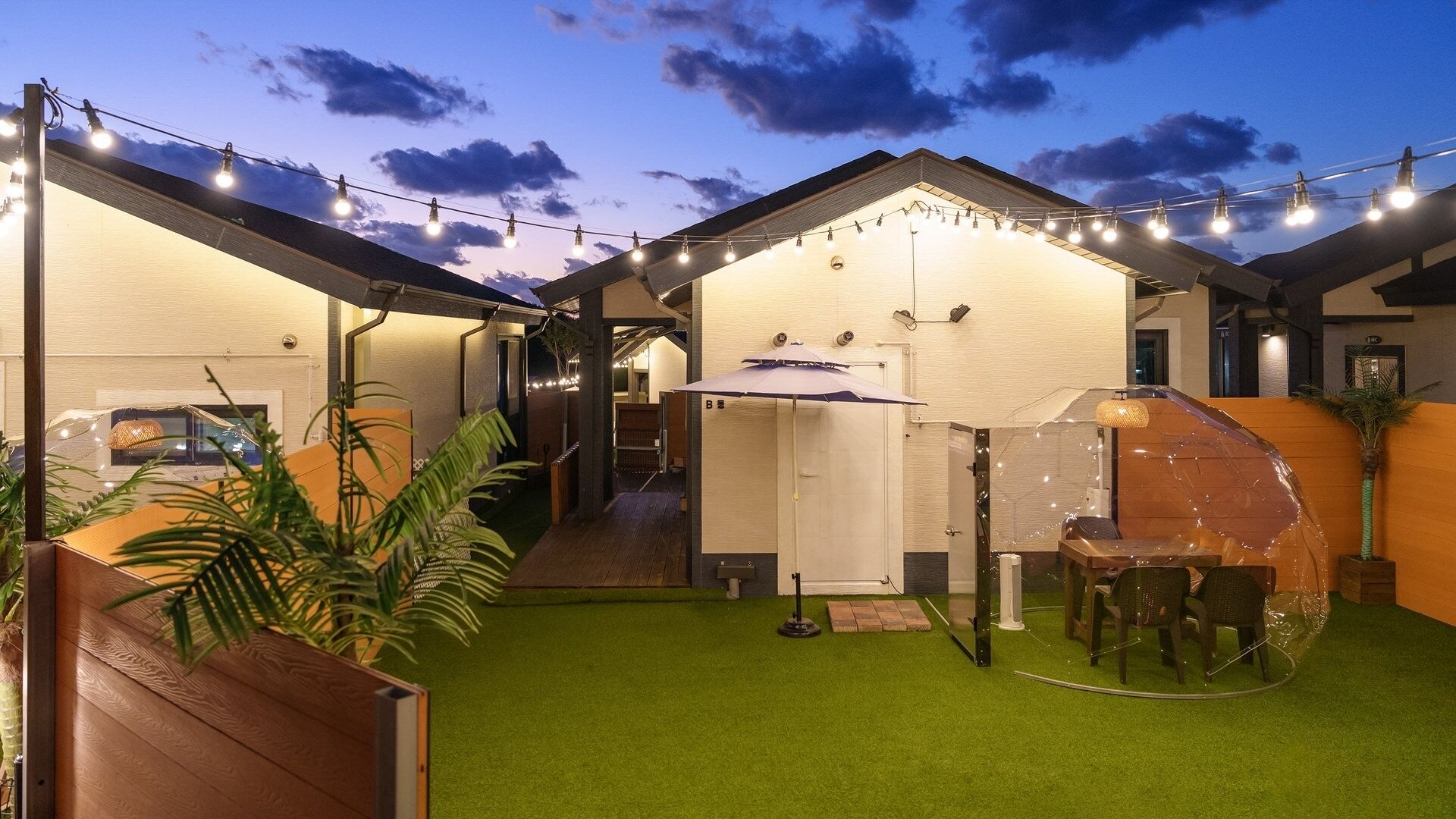 A courtyard with artificial grass, string lights, a covered seating area, and a small table.