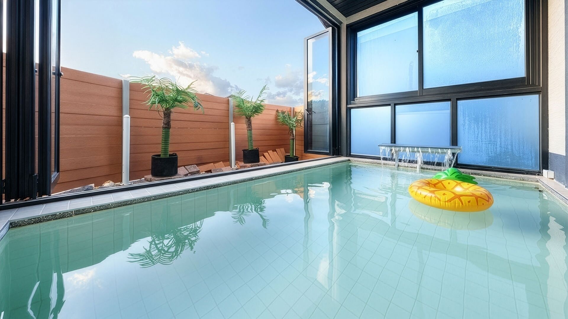 An indoor swimming pool with clear glass walls, wooden paneling, and potted plants.