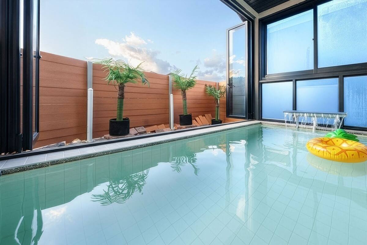 An indoor swimming pool with clear glass walls, wooden paneling, and potted plants.