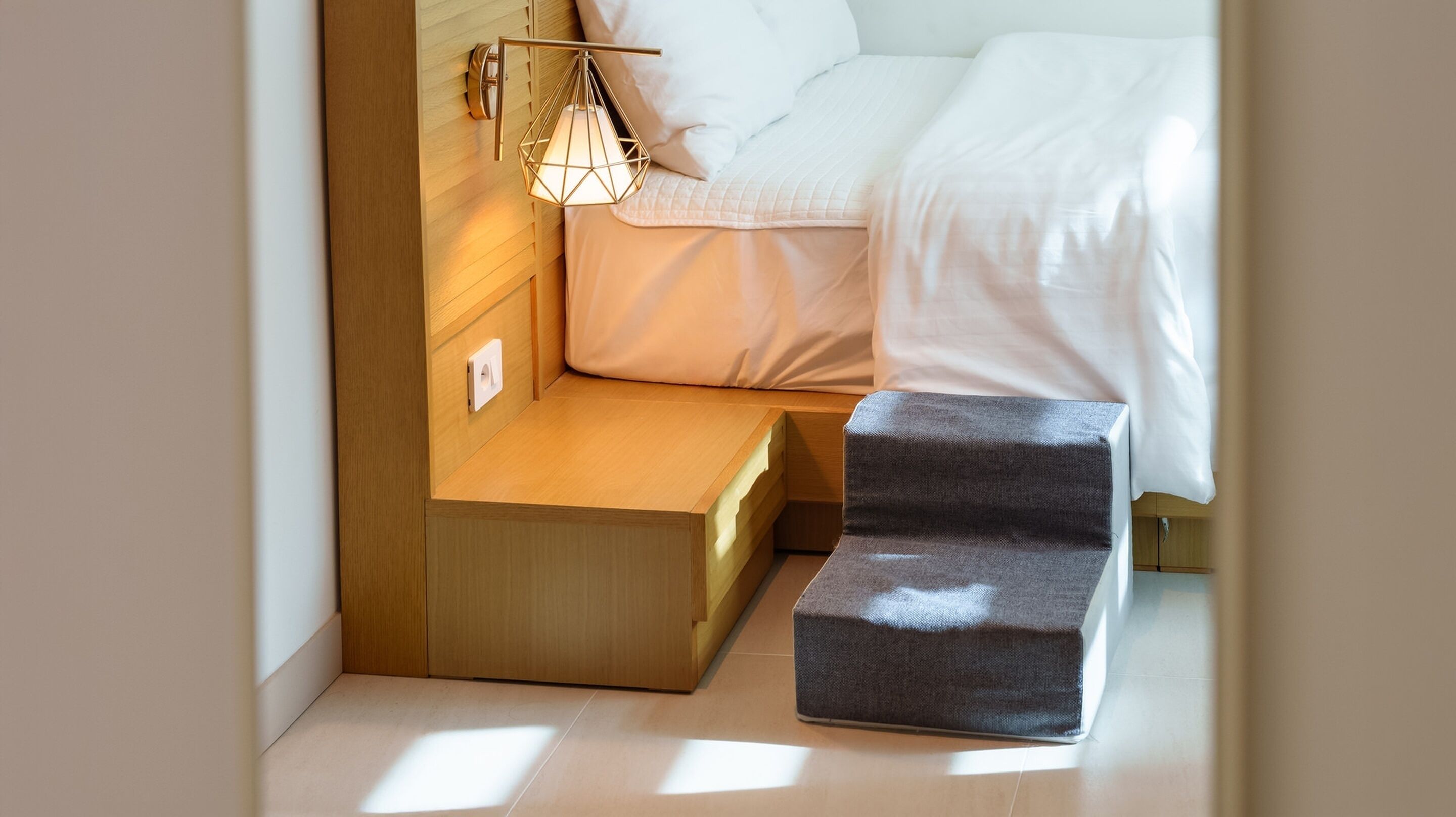 A compact bedroom with a bed, bedside table, and a small stool.