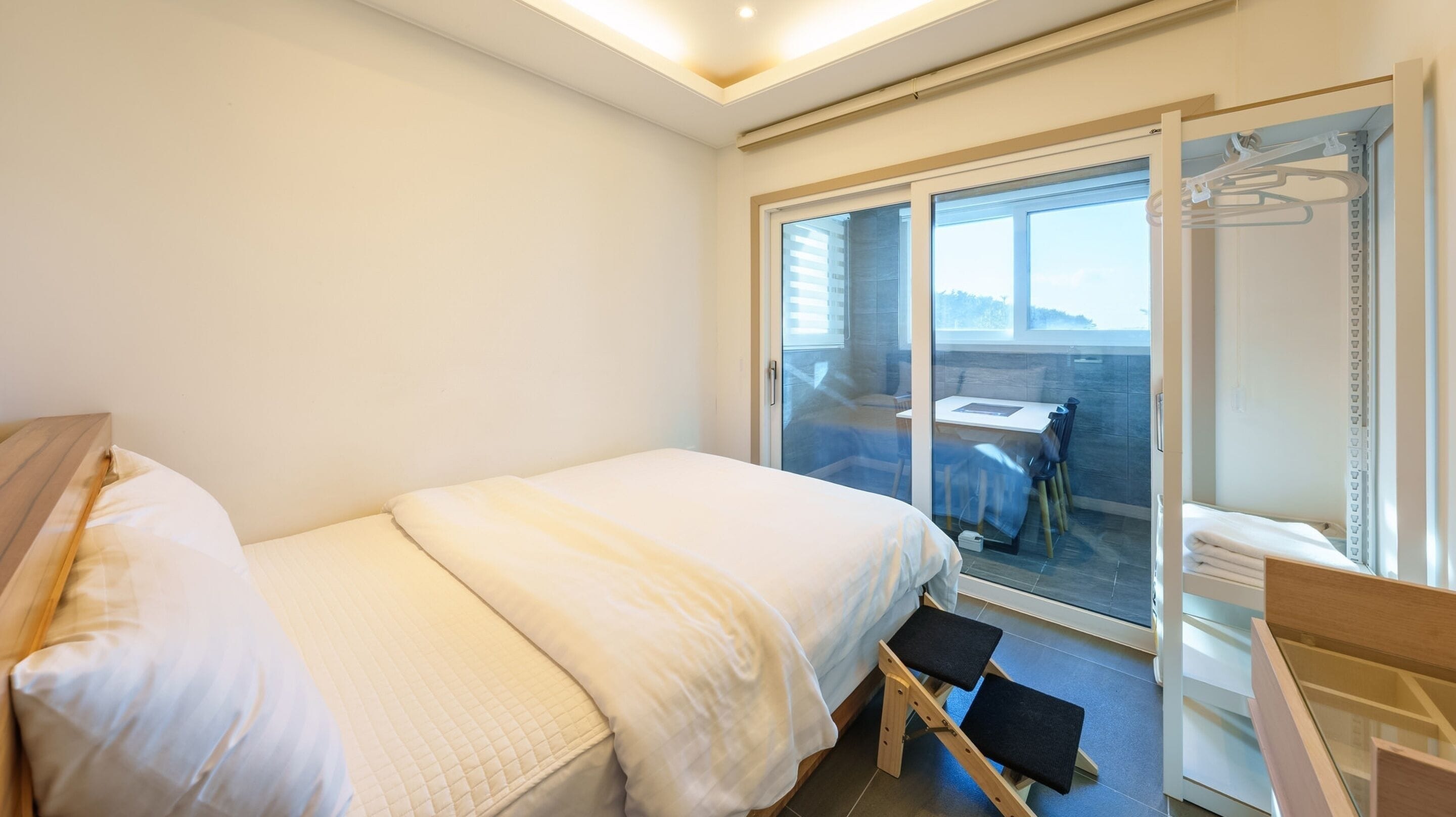 A bedroom with a bed, a small table, and a chair. There is a sliding glass door leading to a balcony.
