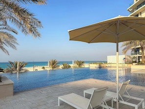 A poolside area with lounge chairs and an umbrella, overlooking a beach and ocean. - Silkhaus Luxury 1BR | Mamsha Saadiyat Sea View (Abu Dhabi)