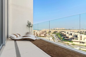 A balcony with a view of a cityscape, a plant, and a seating area with cushions. - Silkhaus Luxury 1BR | Mamsha Saadiyat Sea View (Abu Dhabi)