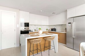 Eine moderne Küche mit weißen Schränken, einem Edelstahl-Kühlschrank, einem Einbauofen und einer Marmorarbeitsplatte.