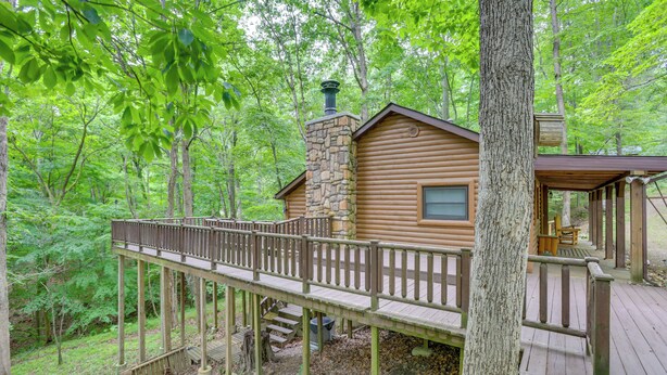 A log cabin with a wooden deck and a stone chimney, surrounded by a forest. - Lake Access & Hot Tub! Serene Rockbridge Cabin (Rockbridge)