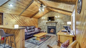 A cozy cabin interior with a stone fireplace, wooden ceiling beams, a leather sofa, and a bar area. - Lake Access & Hot Tub! Serene Rockbridge Cabin (Rockbridge)
