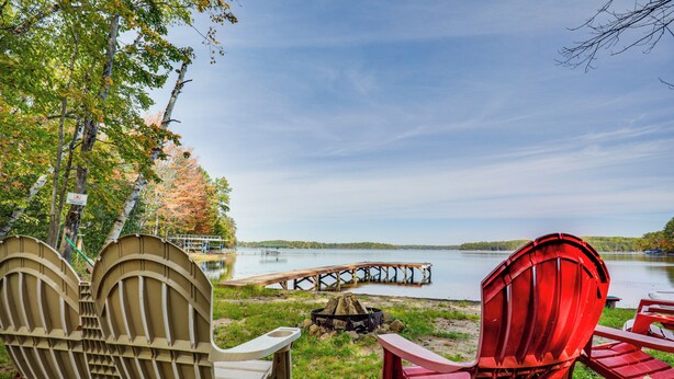 A lakeside setting with Adirondack chairs, a fire pit, and a wooden dock extending into the water. - Land O' Lakes Cabin on Big Portage w/ Fire Pit (Land O' Lakes)
