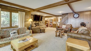 A cozy cabin interior with a stone fireplace, wooden beams, and a large window overlooking a forest. - Land O' Lakes Cabin on Big Portage w/ Fire Pit (Land O' Lakes)