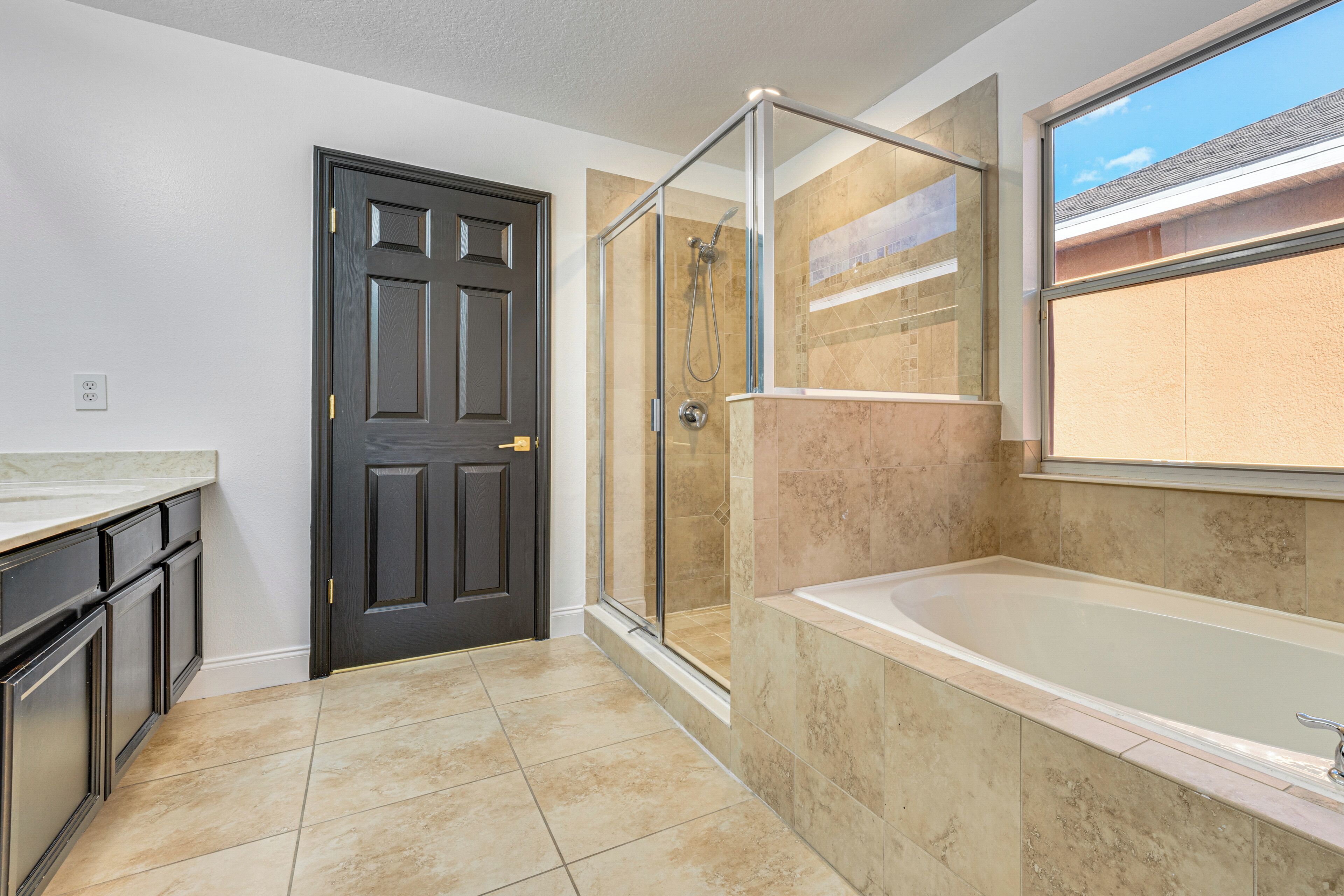 A bathroom with a glass-enclosed shower, a bathtub, and a door with a handle.