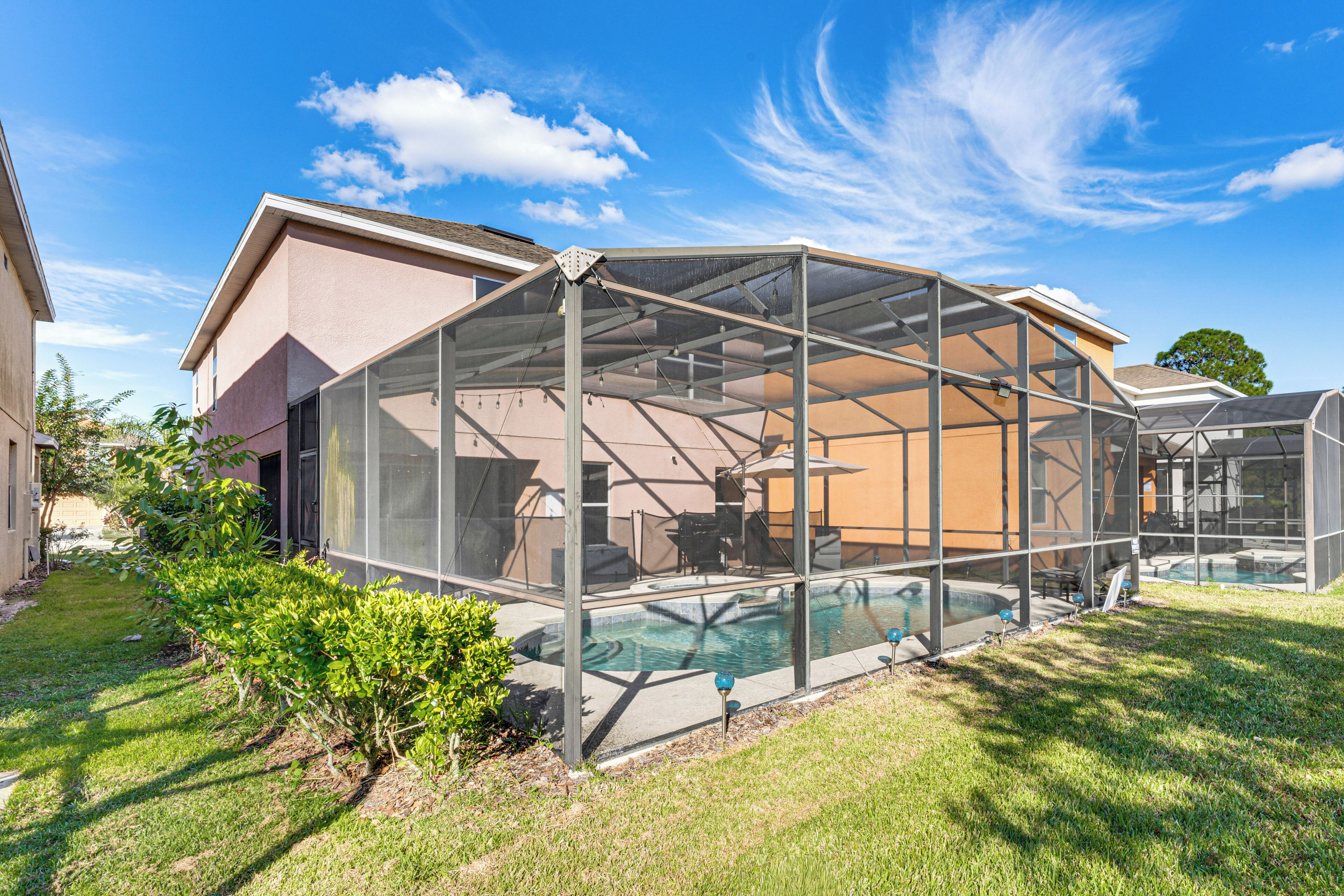 A covered outdoor swimming pool with a glass enclosure, surrounded by a lawn and a house.