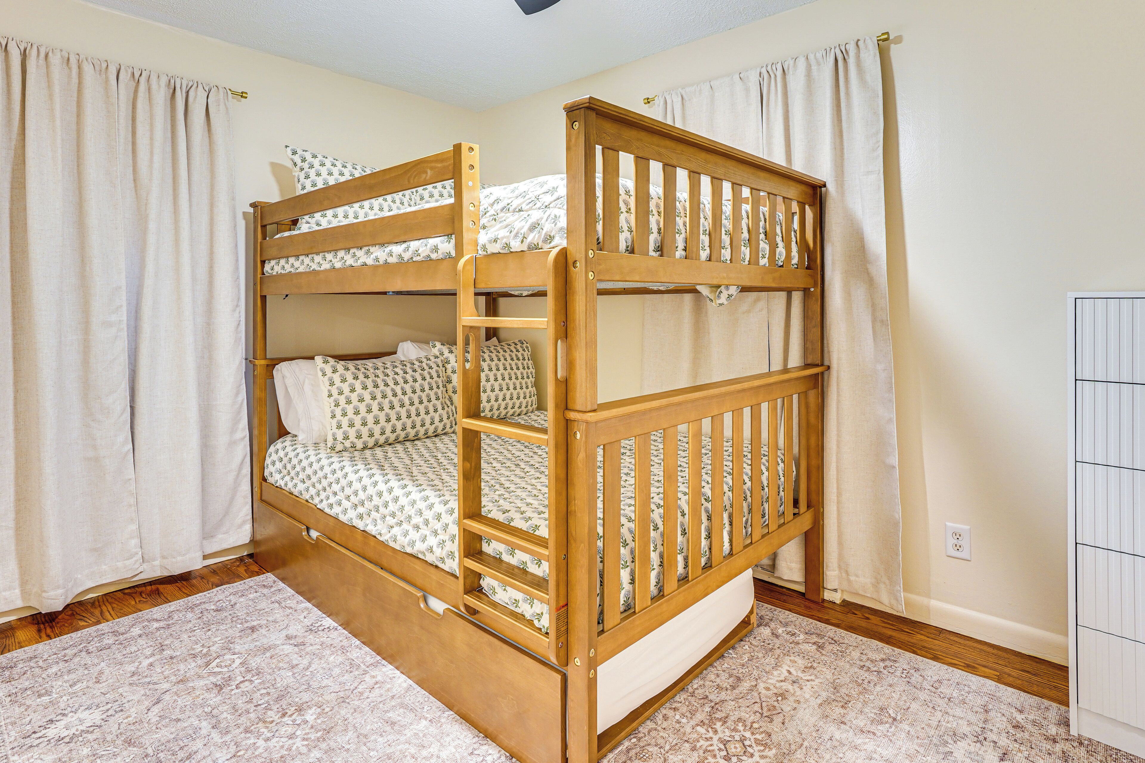 Een stapelbed met houten frame, witte beddengoed en een rug met een patroon.