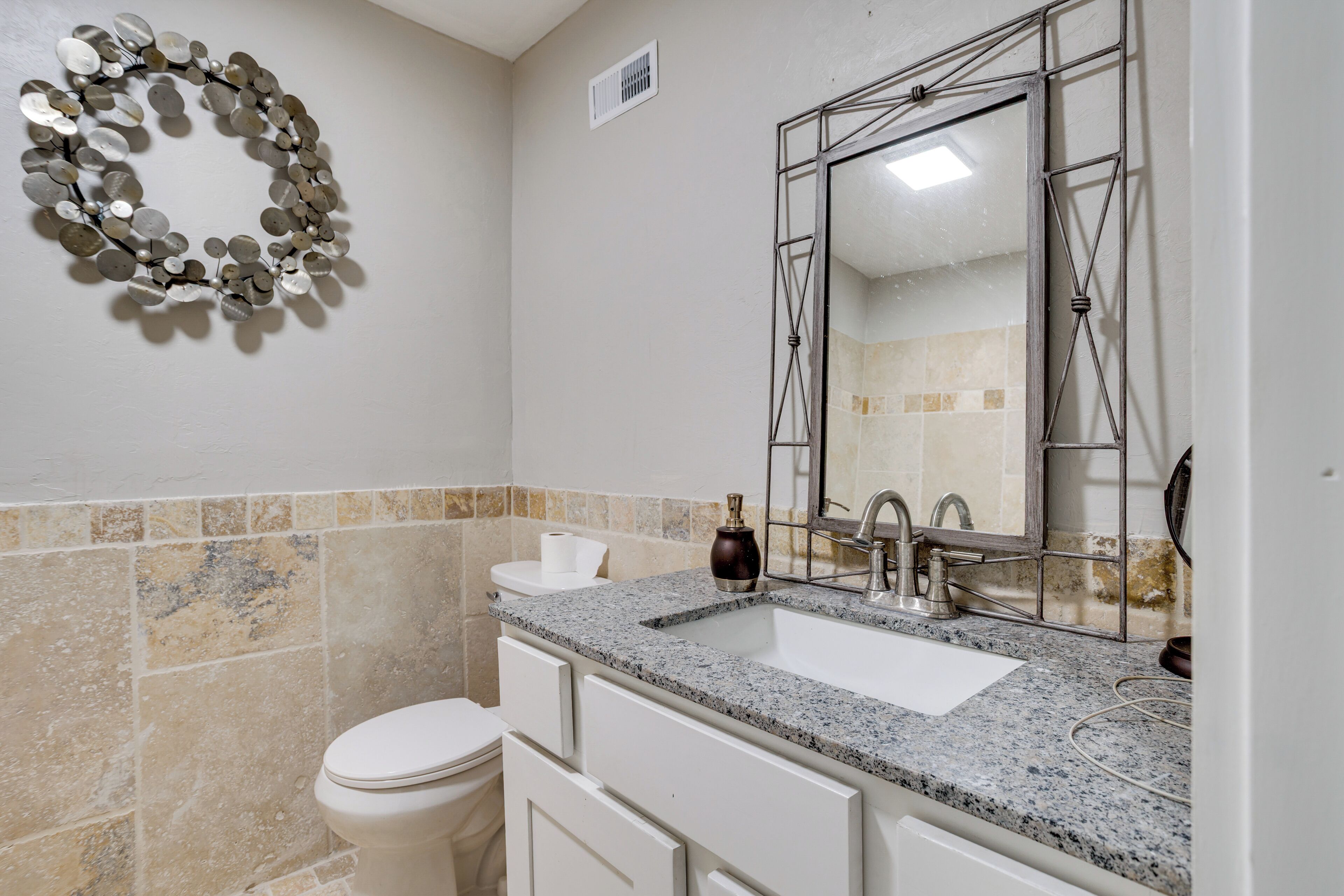 A bathroom with a granite countertop sink, a large mirror, and a decorative wall piece.