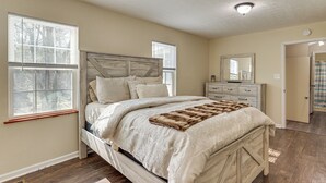 A bedroom with a wooden bed, a dresser, a mirror, and two windows. - 'Doris & Susan's Place' - Historic Tuskegee Home (Tuskegee)