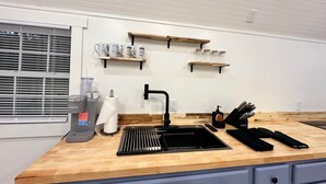 Una cocina moderna con encimera de madera, pileta negra y estantes empotrados.