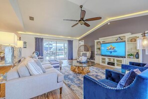 Een moderne woonkamer met een bank, fauteuils, een televisie en een plafondventilator.