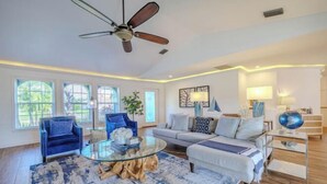 A spacious living room with a ceiling fan, a round glass coffee table, a sofa, and a TV stand. - Cape Coastal (Cape Coral)
