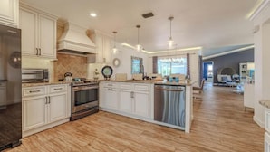 A spacious kitchen with white cabinetry, stainless steel appliances, and a central island. - Cape Coastal (Cape Coral)