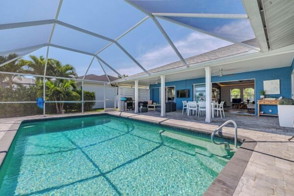 A covered swimming pool with a patio area, a covered seating area, and a view of the outdoors. - Cape Coastal (Cape Coral)