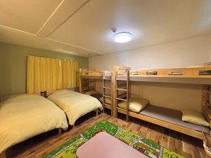 A dormitory room with bunk beds, a window with curtains, a ceiling light, and a colorful rug.