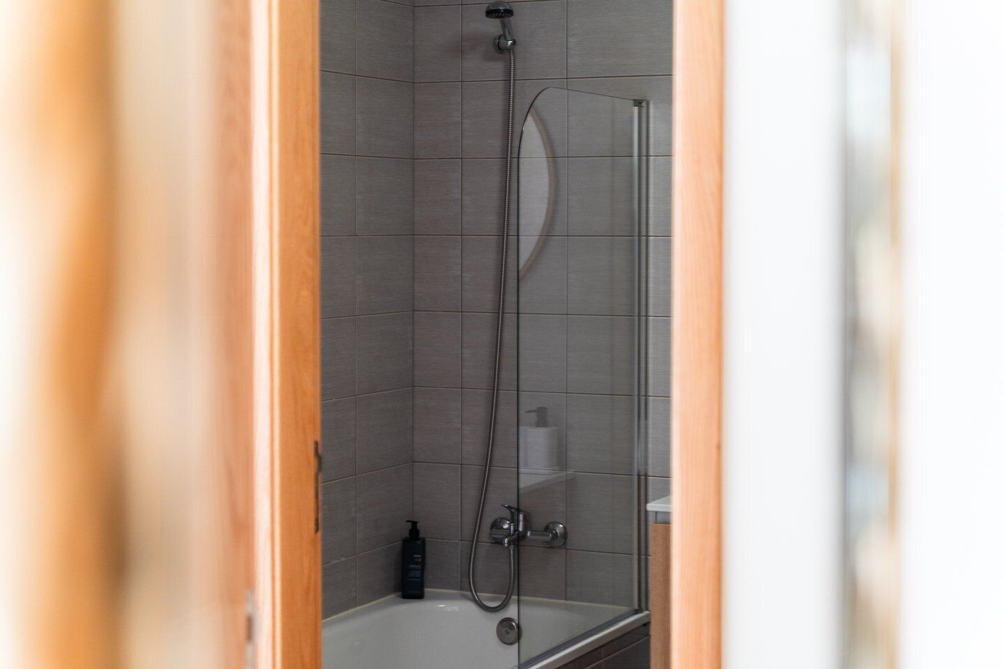 A shower area with a glass enclosure, a handheld showerhead, and a bottle of shampoo.