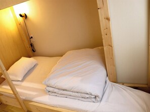 Ein Einzelbett aus Holz mit weißer Bettwäsche, einer Steckdose und einer Wandleuchte.