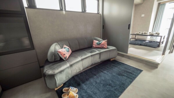 A modern room with a grey sofa, two patterned cushions, a dark blue rug, and a pair of slippers on the floor. - R98BB2E_501 / Taito-ku Tokyo (Taito-ku)